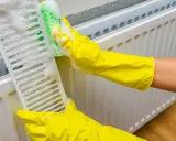 Manos con guantes amarillos limpian la rejilla de un radiador con una esponja y espuma.