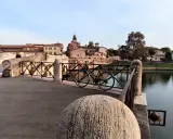 Ponte sul fiume a Borgo San Giuliano, con una bicicletta appoggiata alla ringhiera e palazzi sullo sfondo.