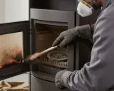 Un technicien en masque et gants effectue la révision du poêle à granulés, brossant l'intérieur pour un nettoyage optimal.