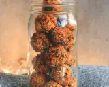 Ein Glas gefüllt mit vielen kleinen, runden Energiebällchen, die mit grünen Kräutern durchsetzt sind.