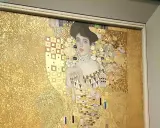 A woman in gold painting, adorned with intricate patterns and jewels, gazes serenely from a gilded background.