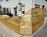 Nybyggt staket i trä ramar in uteplatsen. Grillen och parasollet syns bakom.