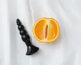 Czarny dildo obok przekrojonej pomarańczy, sugerujący orgazm analny.
