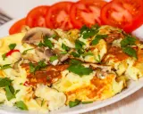 Pyszny omlet jajeczny z pieczarkami i natką pietruszki, podany z plastrami pomidora. Idealny na śniadanie.