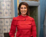 Rania Shemoun Olsson ler i en röd blus med puffärmar. Bakom henne syns en kakelugn och en dörröppning.