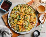 Bunte koreanische Pfannkuchen mit Gemüse, Pilzen und Karotten, serviert mit Dip und Stäbchen.