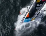 Le voilier de Boris Herrmann fend les vagues, projetant une gerbe d'eau. La voile arbore "Race we must win".