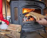 Une main ajoute du bois dans un poêle à bois allumé. Un bon choix de poêle à bois est essentiel pour un hiver chaleureux.