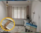 Jasne okna z żaluzjami w środku, ozdobione sznurkiem, tworzą przytulną atmosferę. Obok sztaluga z obrazem plaży.