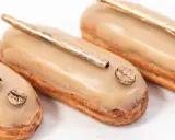 Trois éclairs gourmands, glacés à la crème pâtissière café, ornés d'une touche dorée et d'un grain de café scintillant.