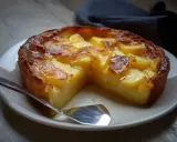 Un délicieux clafoutis pomme, doré et fondant, servi sur une assiette blanche avec une cuillère.