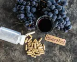 Resweratrol co to? Suplementy w kapsułkach, kieliszek czerwonego wina i winogrona na ciemnym tle.