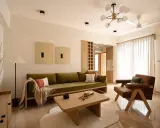 Soggiorno in stile Japandi con divano verde, poltrona in pelle, tavolino in legno e opere d'arte minimaliste.