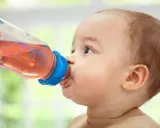 Kleines Baby trinkt aus einer Flasche mit rosafarbenem Tee. Ab wann Tee Baby? Diese Frage stellen sich viele Eltern.