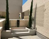 Terraza moderna con cipreses y un retranqueo de fachada que crea un espacio íntimo.
