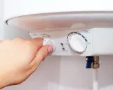 Mano ajustando el dial de potencia de un termo eléctrico. Si el termo pita, puede ser por un ajuste incorrecto de temperatura o por un problema de calentamiento.