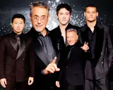 Five men in black suits with black shirts pose for a photo.
