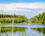 Spokojne jezioro otoczone zielenią, z domkiem na wzgórzu. Idealne miejsce na wypoczynek w okolicach Zielonej Góry.