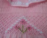 Detalle de puntada smock en tela rosa, con flores bordadas. Aprende como hacer punto smock.