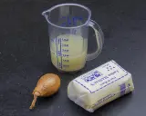 Ingrédients pour un beurre blanc : un oignon, un pichet gradué avec un liquide jaune, et un paquet de beurre Lucien Massaux.