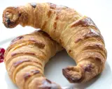 Två gyllene croissants med vaniljfyllning ligger på en vit tallrik. En klick hallonsylt bredvid.