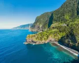 Grüne Berghänge stürzen ins türkisfarbene Meer. Ein perfekter Tag für eine Reise nach Madeira im Oktober.