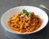 Szybki obiad z makaronem fusilli w kremowym sosie pomidorowym, posypany parmezanem i orzechami, udekorowany listkiem bazylii.