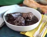 Un plat de coq au vin mijoté, servi dans un bol blanc, avec une fourchette et un couteau à côté.