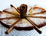 En vacker vit kladdkaka uppskuren i tårtbitar, dekorerad med en pappersros och chokladrullar.