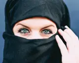 Ein schwarzes Kopftuch umrahmt ein Gesicht, dessen grüne Augen durch den Stoff blicken. Die Bedeutung von Kopftuchfarben ist vielfältig.