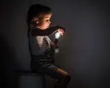 Niña con miedo a la oscuridad, sentada en un rollo de cable, sosteniendo una bombilla encendida.