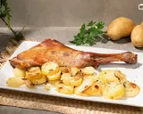 Paletilla de cordero al horno dorada y jugosa, acompañada de patatas panadera y perejil fresco. Un plato principal delicioso.