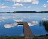 Drewniany pomost na spokojnym jeziorze Urszulewskim, odbijającym błękitne niebo z białymi chmurami.