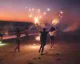 Giovani festeggiano il Ferragosto sulla Riviera Romagnola con scintille sulla spiaggia al tramonto.