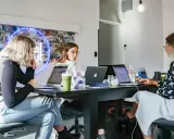 Trzy kobiety pracują przy biurku w nowoczesnym biurze. To zespół agencji kreatywnych, tworzący nowe pomysły.