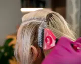 Profesjonalna dekoloryzacja włosów w salonie. Różowa rękawiczka i pędzel nanoszą produkt na blond pasma.