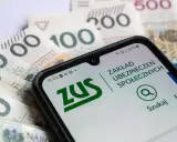 Telefon z aplikacją ZUS na tle polskich banknotów. Sprawdź, jakie odsetki ustawowe obowiązują w bieżącym roku.