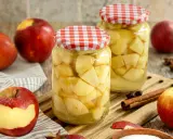 Zwei Gläser mit Apfelstücken, bereit zum Apfel einkochen. Frische Äpfel, Zimtstangen und Sternanis liegen daneben.