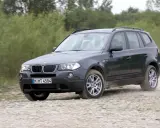 Ciemnoszary BMW X3 2024 na szutrowej drodze, otoczony zielenią.