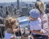 Familia disfrutando de las vistas de Nueva York con niños, explorando la ciudad a través de un telescopio.