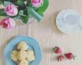 Chouquettes traditionnelles sur une assiette bleue, accompagnées de fraises et d'un bouquet de tulipes roses. Parfait pour une pause gourmande.