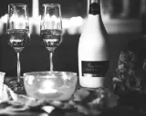 Deux flûtes de champagne pétillant, une bouteille de "Besgane bianc CHAMPAGNE" et des roses, ambiance romantique.