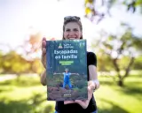 Mujer sonriente muestra libro "Escapadas en familia", con un niño en portada, ideal para viajes inolvidables para niños por España.