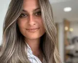 Frau mit langen, welligen Haaren in Balayage-Optik, aschblond mit helleren Strähnen. Ihr Blick ist warm und einladend.