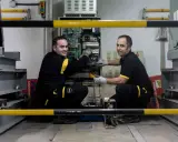 Técnicos realizan mantenimiento de elevadores en un taller, revisando la electrónica y cableado.