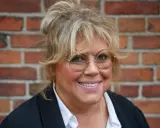Marie Nilsson Lind ler mot kameran, med sitt blonda hår uppsatt och runda glasögon.