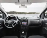 Interior del Dacia Lodgy con volante, pantalla táctil y palanca de cambios. El paisaje marino se ve a través del parabrisas.