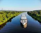Nave da crociera solca un fiume sereno, con rive alberate che ricordano la bellezza naturale vicina alla capitale Russia.