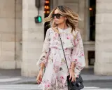 Frau mit luftgetrockneten, gesunden Haaren, die im Wind wehen, trägt ein Blumenkleid und Sonnenbrille.