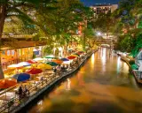 Bunte Sonnenschirme säumen den River Walk in San Antonio, wo Gäste abends in Restaurants am Wasser speisen.